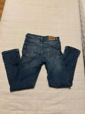 Blå Replay jeans bootcut - Säljer ett par klassiska blå jeans från Replay med bootcut passform. Jeansen har fem fickor, snygga slitningar och Replay-logga på bakfickan samt vid linningen. Tillverkade i slitstarkt denim med kontrastsömmar och knappgylf.