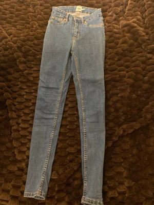 Blå skinny jeans från 157, storlek S - Säljer ett par klassiska blå skinny jeans från 157 med hög midja. Jeansen har fem fickor, gul kontrastsöm och raka bakfickor. Materialet är stretchigt jeans och passformen är tight hela vägen ner. Perfekta till sneakers eller boots.