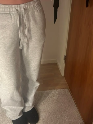 Grå mjukisbyxor med snörning - Säljer ett par ljusgrå mjukisbyxor med resår i midjan och snörning. Byxorna har normal passform, raka ben och sidofickor. Perfekta för chill dagar hemma eller när du vill vara bekväm. Tillverkade i mjukt bomullsmaterial.