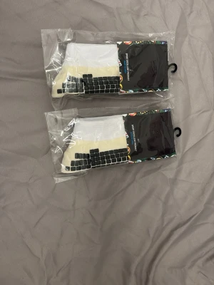 Typ skillsocks - Bilden visar två par vita strumpor med svarta halkskydd, förpackade i plast. Ingen väst syns på bilden.