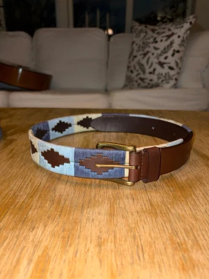 Blå-vitt broderat bälte - Helt nytt och inplastat mörk blått och vitt färgat broderat bälte i färgerna: mörkblå och ljusblå och vit. Extremt fräscht bälte som ger din outfit en sista detalj. Finns 5 olika storlekar att välja mellan: 80-110 cm. Hör av er vid minsta fundering!