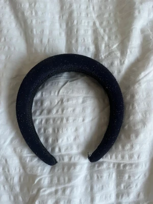 Mörkblått glittrigt hårband - Säljer ett mörkblått, brett hårband med glittrig yta som ger en snygg touch till din look. Perfekt accessoar för att lyfta vilken outfit som helst. Hårbandet är vadderat och sitter bekvämt på huvudet.
