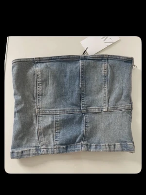Ljusblå denim tubtopp från Zara - Trendig ljusblå tubtopp i denim från Zara. Toppen har en patchwork-design med synliga sömmar och dragkedja i sidan för enkel påklädning. Perfekt att styla med höga jeans eller kjol för en cool look. Aldrig andvönt