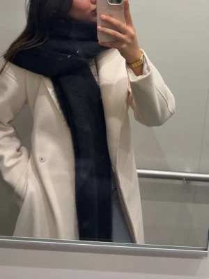 Beige kappa med bälte och bred krage - Säljer en snygg beige kappa med bred krage och knytskärp i midjan. Kappan har en klassisk omlottmodell och är tillverkad i ett mjukt ullmix-material. Perfekt för dig som vill ha en stilren och tidlös look under höst och vinter.