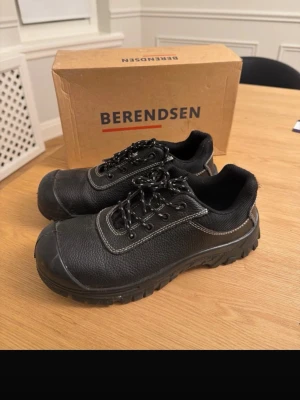 Svarta Toe Guard arbetsskor - Robusta svarta arbetsskor från Toe Guard med slitstark ovandel i skinn och detaljer i textil. Skorna har kraftig sula, snörning med reflexdetaljer och förstärkt tåparti. Perfekta för dig som vill ha stabilitet och skydd på jobbet.