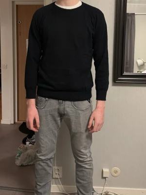 Svart långärmad stickad tröja från Melawear - En enkel svart stickad tröja från melawear med rund hals och långa ärmar. Tröjan har ribbade muddar vid ärmslut och nederkant, vilket ger en klassisk och clean look. Perfekt att slänga på sig under kyligare dagar. (Jag är 190cm) den är kort i armarna på mig men annars sitter den rätt bra men skulle inte rekommendera tröjan till någon under 190