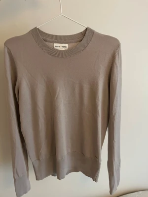 Beige stickad tröja  - Beige stickad tröja från Holly & White med rund halsringning och långa ärmar. Tröjan har ribbade muddar och dekorativa guldfärgade knappar vid ärmsluten. 