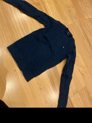 Mörkblå kabelstickad tröja från Gant - Säljer en mörkblå kabelstickad tröja från Gant i stretchig bomull. Klassisk rund halsringning och diskret Gant-logga broderad på bröstet. Perfekt till höst och vinter för en clean och stilren look.