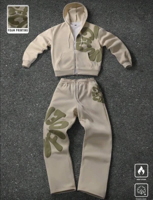 Beige fleecedress med camouflage - Snygg beige fleecedress med grönt camouflage-mönster i foam print på ena sidan. Västen har dragkedja framtill och en avslappnad passform. Perfekt för dig som vill sticka ut med en unik detalj och hålla dig varm.