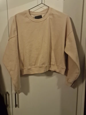 Ljusrosa croppad sweatshirt - Säljer en ljusrosa croppad sweatshirt med rund hals och långa ärmar. Tröjan har en relaxed passform och ribbade muddar vid ärmslut och nederkant. Perfekt för dig som gillar en enkel och clean stil.