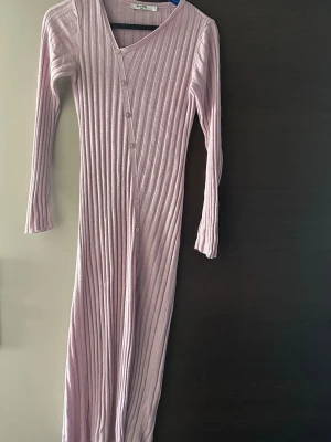 Ljuslila ribbad långklänning NA-KD - Supersnygg ribbad långklänning från NA-KD i ljuslila. Klänningen har v-ringning, långa ärmar och knappar framtill i omlottstil. Perfekt för dig som gillar en stilren och trendig look.