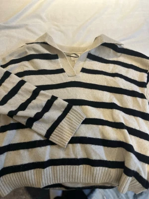 Randig beige och svart tröja H&M - Säljer en beige och svart randig tröja från H&M i storlek M. Tröjan har en krage, v-ringning och långa ärmar. Materialet är mjukt och stickat, perfekt för lager på lager under höst och vinter.