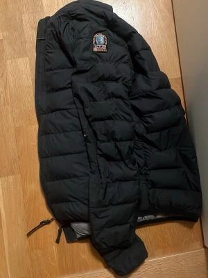 Svart pufferjacka från Parajumpers - Säljer en svart pufferjacka från Parajumpers med patch på ärmen. Jackan har dragkedja framtill och två sidofickor med dragkedja. Perfekt för kalla dagar och har en klassisk, sportig look.