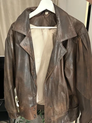 vintage oversize läderjacka - Säljer en brun läderjacka i oversize modell med bred krage och tryckknappar. Jackan har en cool retrovibe och är tillverkad i äkta läder med ljus insida. Perfekt för dig som vill ha en unik och tidlös look.