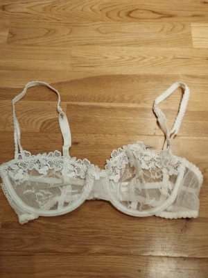NY Vit spets-bh med blommor från Passionata - Säljer en superfin vit bh från Passionata med blommig spets och transparent mesh. Aldrig använd med saknar tags. Bh:n har tunna axelband och vackra broderade detaljer som ger en romantisk vibe. Perfekt för alla hjärtans dag  / Valentine's day. Jag har fler annonser uppe och ger mängd rabatt, så kolla gärna min sida!