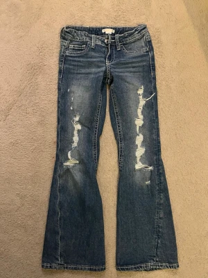 Blå bootcut jeans med slitningar - Säljer ett par justerbara blåa jeans med bootcut passform ifrån Gina tricot young i storlek 146❤️ Jeansen har hål där fram och fickor med broderi, du får betala frakten! nypris: 399kr