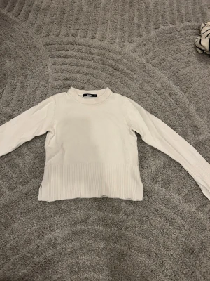 Vit ribbad stickad tröja Bik Bok  - Säljer en enkel och clean vit stickad tröja från Bik Bok i storlek XS. Tröjan har ribbade detaljer vid nederkant och ärmslut, samt en klassisk rund halsringning. Perfekt till lager på lager under höst och vinter.