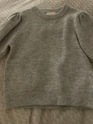 Grå stickad tröja Gina Tricot - Mysig grå stickad tröja från Gina Tricot med puffärm. Aldrig använd. Ser kort och stor men när man har på sig den är den bättre super bra kvalité inge hål eller smutts någon stans. Pris kan andras på bra förslag 