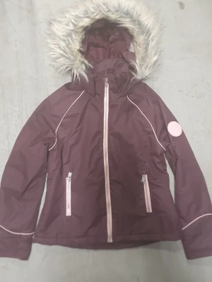 Vinterjacka - Snygg lila vinterjacka från H&M med avtagbar huva och fuskpäls. Jackan har ljusrosa dragkedjor, två fickor fram och en cool patch på ärmen med texten 'Support Your Local Girl Crew'. Perfekt för kalla dagar och riktigt skön passform.