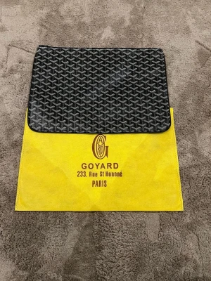 Svart kuvertväska  - Snygg svart kuvertväska med ikoniskt grafiskt mönster i vitt och grått. Väskan har dragkedja upptill och klassisk rektangulär form. Perfekt för att bära det viktigaste och ger en lyxig touch till din outfi