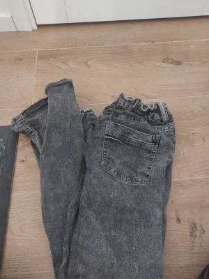 Grå tvättade jeans med resårmidja - Säljer ett par grå tvättade jeans med resår i midjan och klassiska bakfickor. Jeansen har en avslappnad passform och är tillverkade i ett mjukt denimtyg. Perfekta för en chill och bekväm stil.