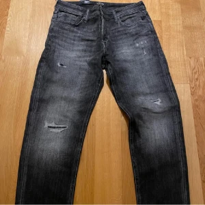 Svarta slitna jeans  - Snygga svarta jeans  med slitningar och lätt tvättad look. Jeansen har klassisk femficksdesign, raka ben och normal passform. Perfekta för dig som gillar en lite ruffare stil. Materialet är jeans i bomull med lite stretch för extra komfort.