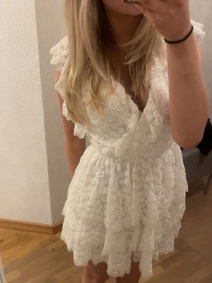 Vit spetsklänning från Nelly - Supersöt vit spetsklänning från Nelly med omlott och volangdetaljer. Klänningen har v-ringning, kort ärm med volang och flera lager i kjolen för en fluffig look. Perfekt till studenten! Ganska stor i storleken, passar mig som har xs/s. Endast använd en gång🌸🌸
