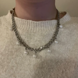 Silverfärgat halsband med pärlor - Snyggt halsband i silverfärgad metall med grov kedja och hängande vita pärlor. Perfekt för dig som vill ha en cool men ändå elegant detalj till din outfit. Kedjan har ett chunky utseende och pärlorna ger en lyxig touch.  Rostfritt och handgjort 