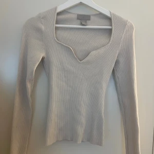 Beige ribbad långärmad topp H&M - Säljer en beige ribbad topp från H&M i storlek XS. Toppen har lång ärm, v-ringad hals med unik form och är figurnära. Materialet är mjukt och stretchigt, perfekt för en clean och stilren look. Passar dig som gillar enkla men snygga detaljer.
