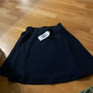 Mörkblå strukturerad kjol Jyothi S - Säljer en mörkblå kortkjol från Jyothi i storlek S. Kjolen har en cool strukturerad yta och en lätt A-linjeformad siluett. Perfekt för dig som gillar stilrena plagg med lite extra textur. Elastisk midja för skön passform.