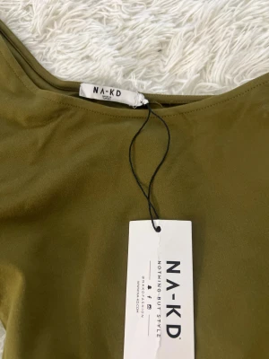 Khakigrön oneshoulder croppad topp NA-KD - Säljer en khakigrön croppad topp från NA-KD i storlek XS. Modellen har en puffärm på ena sidan och är oneshoulder, vilket ger en cool och trendig look. Materialet är mjukt och stretchigt, perfekt för att sticka ut med en unik siluett.