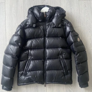 Svart Moncler pufferjacka med huva - Säljer en svart pufferjacka från Moncler som är riktigt varm och skön för vintern. Jackan har dessutom en fungerande NFC-tag. Perfekt för kalla dagar 🙌                