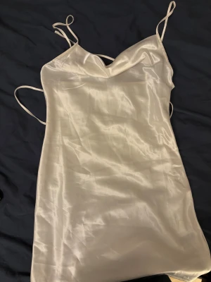 Studentklänning - Säljer en vit kortklänning från H&M Divided i satin storlek xs. Man kan knyta den baktill med banden för att få en figurnära passform, snatched midja. Perfekt för studenten, använd 1 gång 