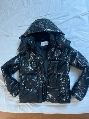 Svart Calvin Klein jacka - Säljer min glansiga Calvin Klein jacka då den har blivit för liten för mig. Jag köpte den för 2200 kr och den har inga skador eller så. Hör av er vid fler frågor💞