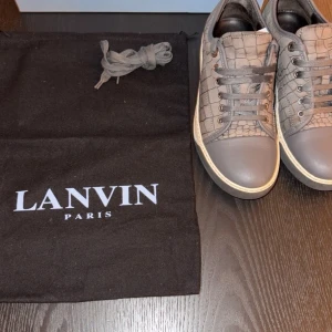 sneakers  Lanvin - Snygga grå sneakers från Lanvin med crocomönstrad mocka och detaljer i slätt skinn. Skorna har rund tå, snörning och vit sula. Perfekta för dig som gillar exklusiv och stilren design med en twist.