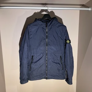  Stone Island windbraker - Snygg marinblå vindjacka från Stone Island med huva och ikonisk patch på vänster ärm. Jackan är inredd med bomull vilket gör att den också håller bra värme. Hör av dig via dm vid frågor eller funderingar 😁