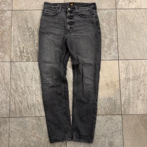 Ler Jeans - Snygga svarta jeans från Lee, modell Austin, med klassisk femficksdesign och raka ben. Jeansen har en mörk tvätt och Lee-logga på bakfickan samt läderpatch i midjan. Jeansen är nästan oanvända. Hör av dig vid frågor!