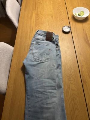 Replay anbass - Säljer ett par ljusblå jeans från Replay med klassisk femficksdesign och snygga slitningar. Jeansen har tapered passform, normal midja och är tillverkade i mjukt jeansmaterial. Läderpatch med Replay-logga bak i midjan och diskreta detaljer på fickorna. Bara skriva vid frågor!