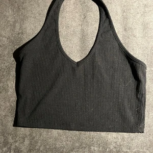 Svart ribbad croppad linnetopp - Säljer en svart croppad linnetopp med ribbad struktur och v-ringad hals. Toppen är ärmlös och har en sportig, stilren look som passar perfekt till jeans eller kjol. Materialet känns mjukt och stretchigt, vilket gör den skön att bära hela dagen.