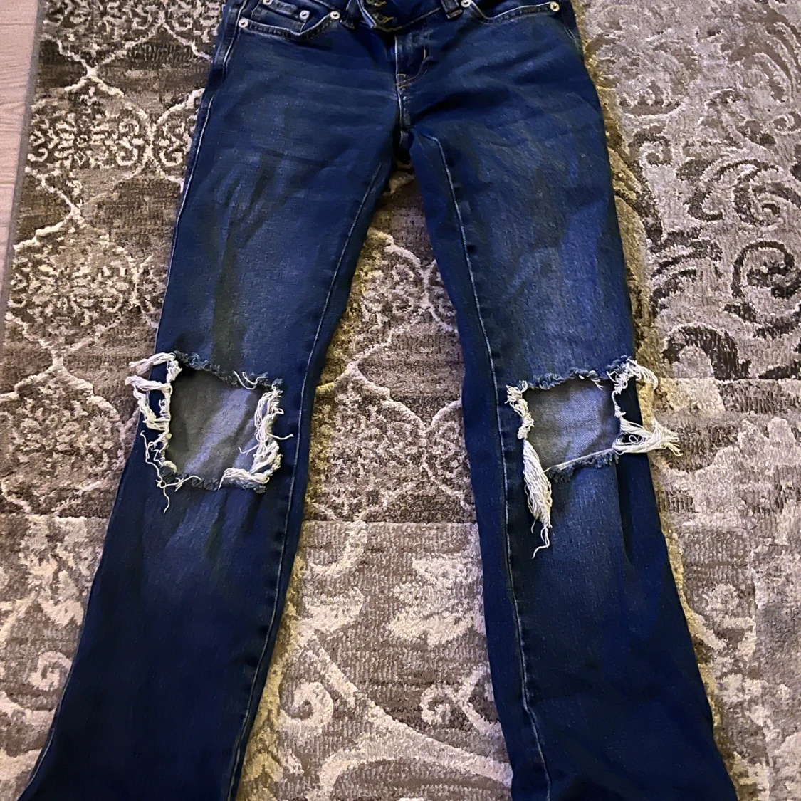 Blå jeans med stora hål vid knäna