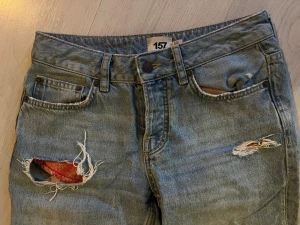 Ljusblå jeans med slitningar och patch - Säljer ett par ljusblå jeans från 157 med coola slitningar och röda patchdetaljer på låren och bakfickan. Modellen har hög midja, raka ben och fransiga benslut. Perfekt för dig som gillar en avslappnad och trendig streetstil.