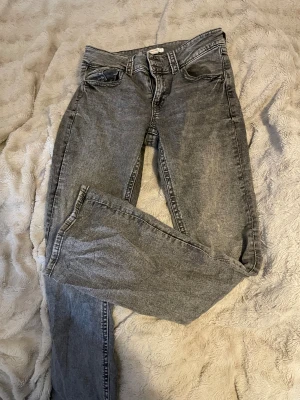 Grå straight jeans med tvättad look - Snygga grå jeans med tvättad finish och klassisk femficksdesign. Modellen har rak passform och normal midja, vilket ger en chill och tidlös vibe. Jeansen är tillverkade i denim och har knappar och dragkedja framtill.