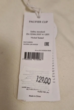 Blommigt nappband med träklämma - Snyggt nappband Blue Garden från Elodie med blommigt mönster i blått, brunt och beige. Bandet är tillverkat av återvunna material och har en rund, guldig träklämma samt vit detalj vid fästet. Perfekt accessoar för att hålla nappen nära till hands. Ny med prislapp kvar o nypris 129 kr.