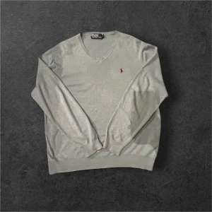 Ljus blå v-ringad tröja från Polo Ralph Lauren - Snygg ljus blå v-ringad tröja från Polo Ralph Lauren med klassisk röd broderad logga på bröstet. Tröjan är långärmad och har ribbade muddar vid hals, ärmslut och nederkant. Perfekt för dig som gillar stilrena och tidlösa plagg.