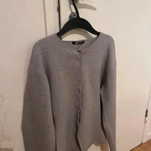Grå kofta från Gina Tricot XS - Snygg grå kofta från Gina Tricot i storlek XS. Koftan har rund hals, långa ärmar och knappar hela vägen framtill. Materialet är mjukt och stickat, perfekt för att slänga på sig när det är lite kyligt ute.