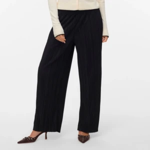 Svarta plisserade wide byxor Vero Moda - Svarta plisserade byxor från Vero Moda i loose fit och wide modell. Byxorna har hög midja och ett snyggt veckat tyg som ger en cool och modern vibe. Perfekta att styla med sneakers eller klackar för en trendig look.