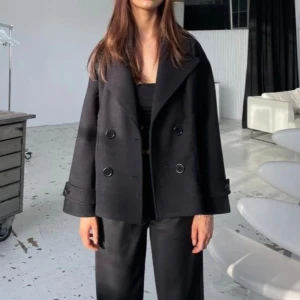 Svart kappa Design by si - Snygg svart kappa med bred krage och dubbelknäppning framtill. Jackan har stora fickor och dekorativa knappar på ärmsluten. Knappt använd. Bilderna är från hemsidan! ❤️