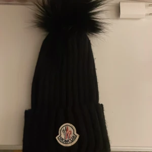 Svart  mössa med pälsboll - Snygg svart ribbstickad mössa med stor pälsboll perfekt för kalla dagar när du vill ha både stil och värme. Inga skador och skriv gärna för fler bilder! 💕