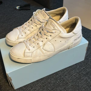 Vita Philippe Model sneakers i skinn - Jätte rena och fina och har användidts bra och försiktigt. Snygga vita sneakers från Philippe Model med klassisk låg profil och rund tå. Skorna är tillverkade i mjukt skinn och har snörning framtill samt en platt sula i svart. Diskret logga på sidan och tungan ger en exklusiv vibe. Perfekt för dig som gillar stilrena och lyxiga sneakers.