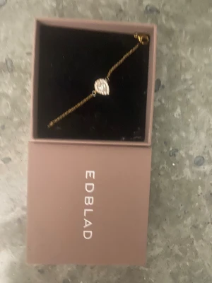 Guldigt armband med droppformad sten från Edblad - Snyggt och stilrent armband från Edblad i guldton med en droppformad, glittrig sten i mitten. Perfekt accessoar för att lyfta din outfit med lite extra bling. Kommer i original ask. Går ej att köpa i butik längre. Fler bilder är det bara att be om🥰